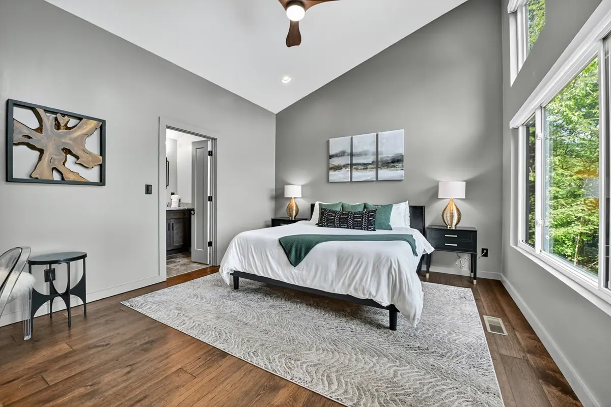 King bedroom with crisp white linens, a soft grey rug and tall windows facing the trees.