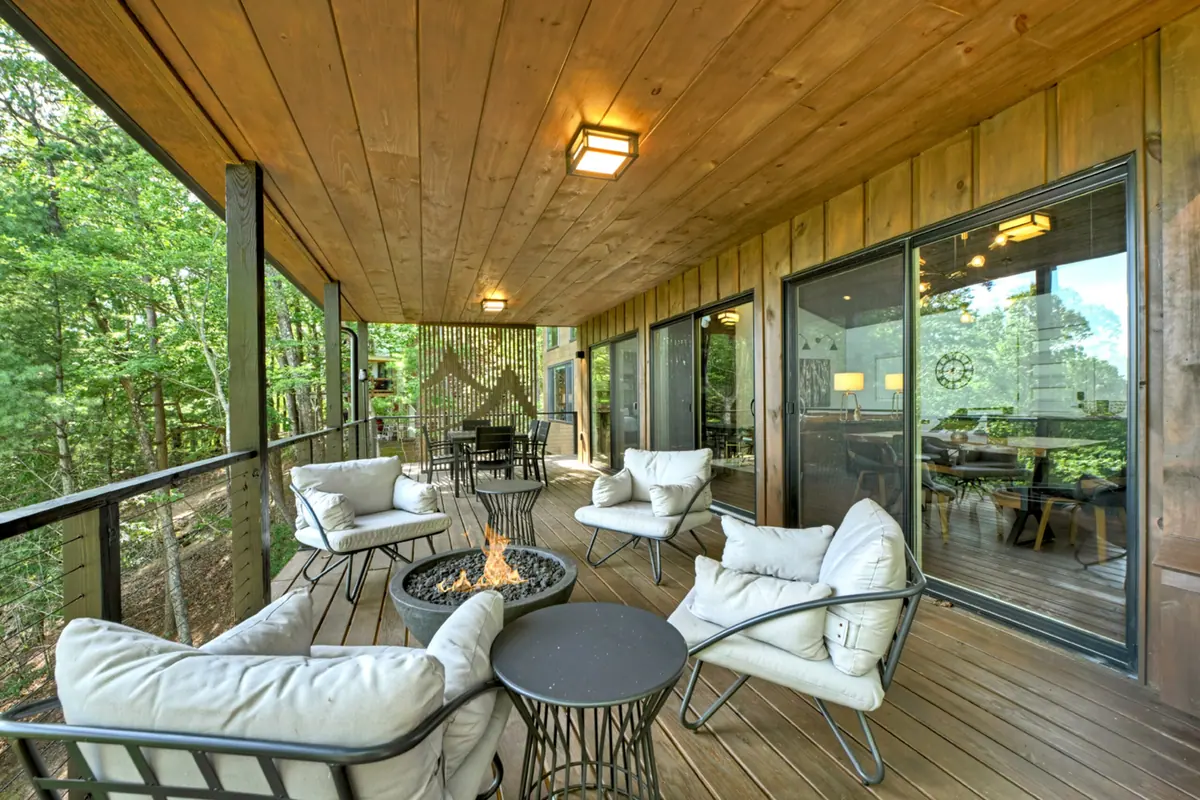Covered deck with cushioned lounge seating and a low fire table, looking out into the surrounding treetops.