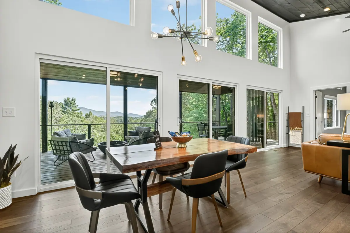 Live-edge dining table beneath a sputnik chandelier, facing a wall of glass sliders that open onto the deck with layered blue mountain ridges beyond.