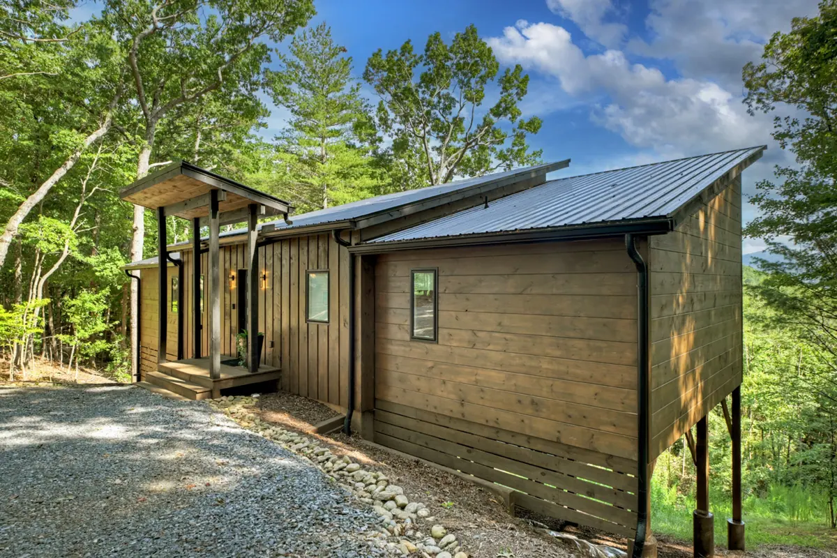 The cabin exterior in vertical cedar siding with a low modern roofline, seen from the gravel drive.
