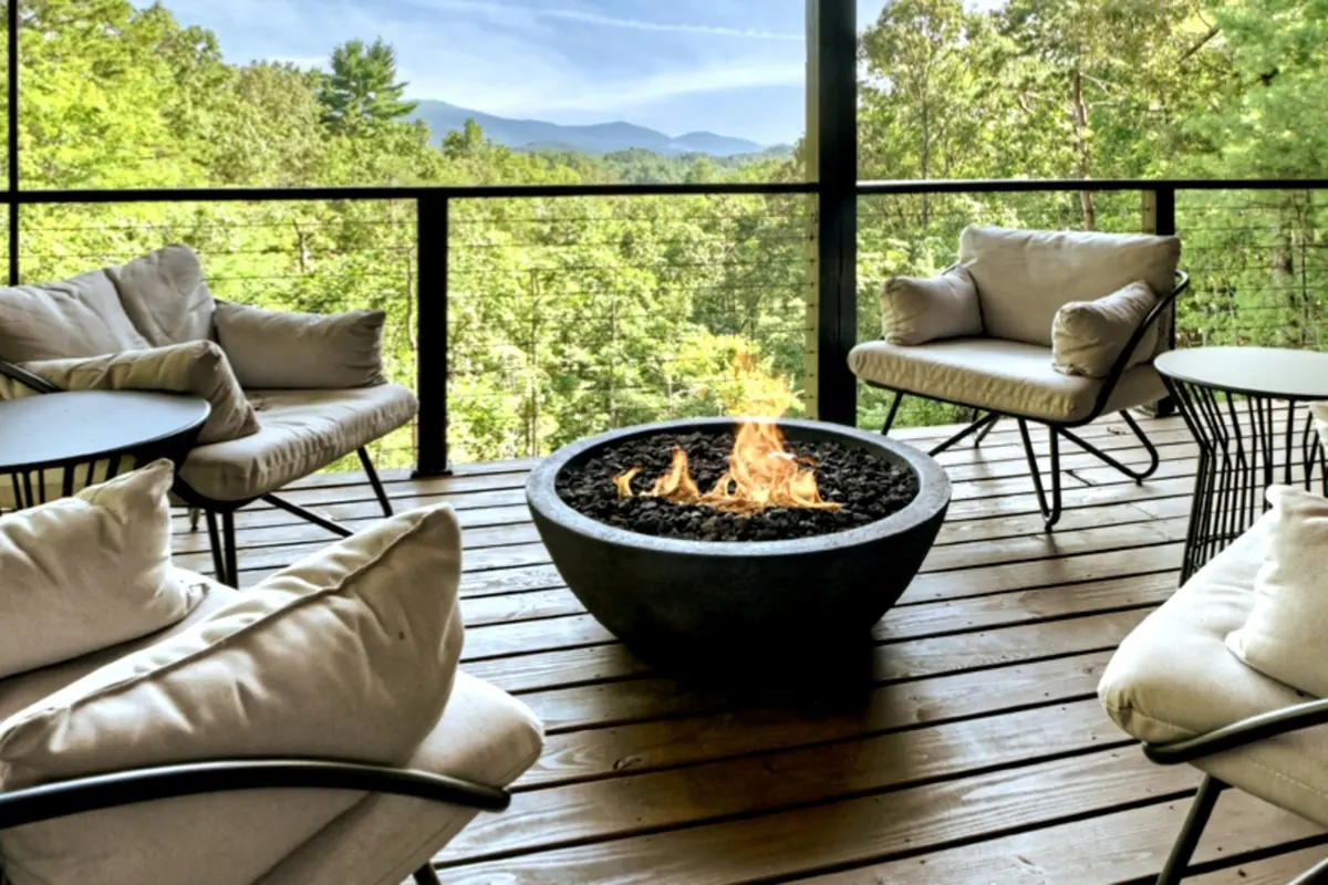 Round gas fire bowl on the upper deck, ringed by lounge chairs with the forest rising behind.