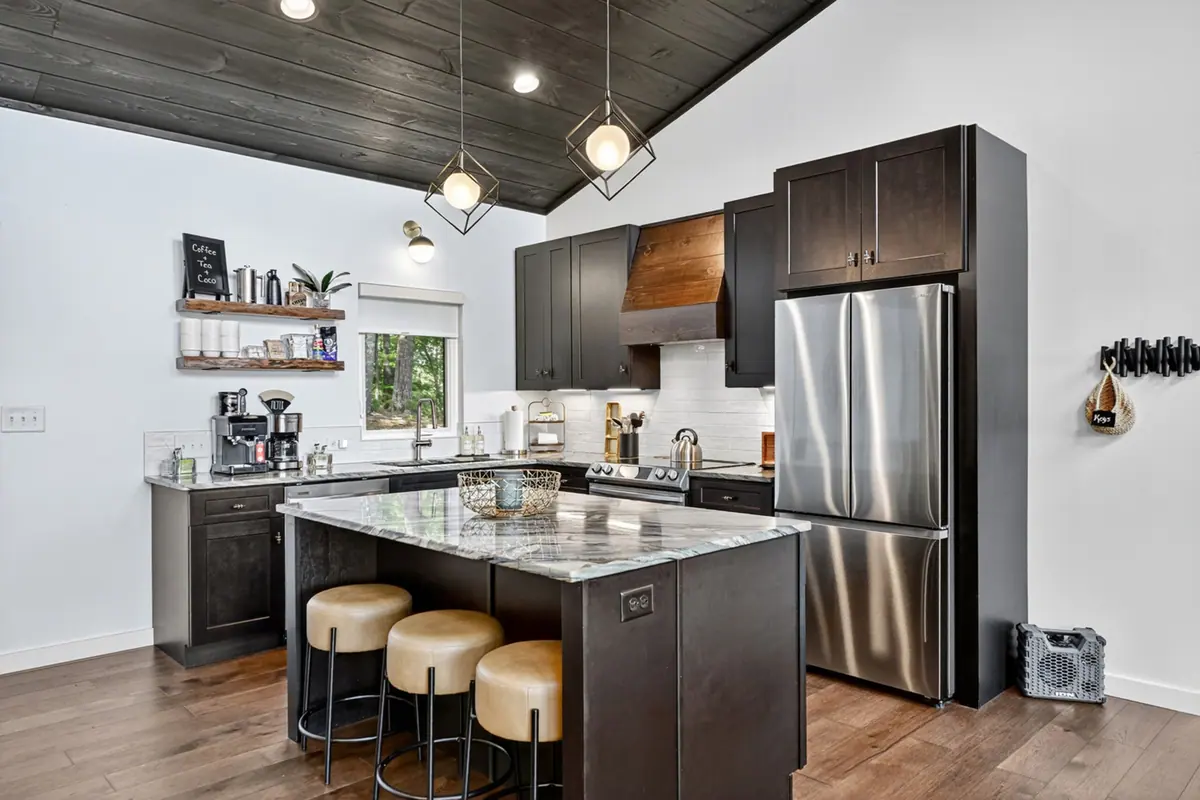 Kitchen with dark cabinetry, a marble-topped island with three leather stools, stainless appliances and an espresso station on floating shelves.