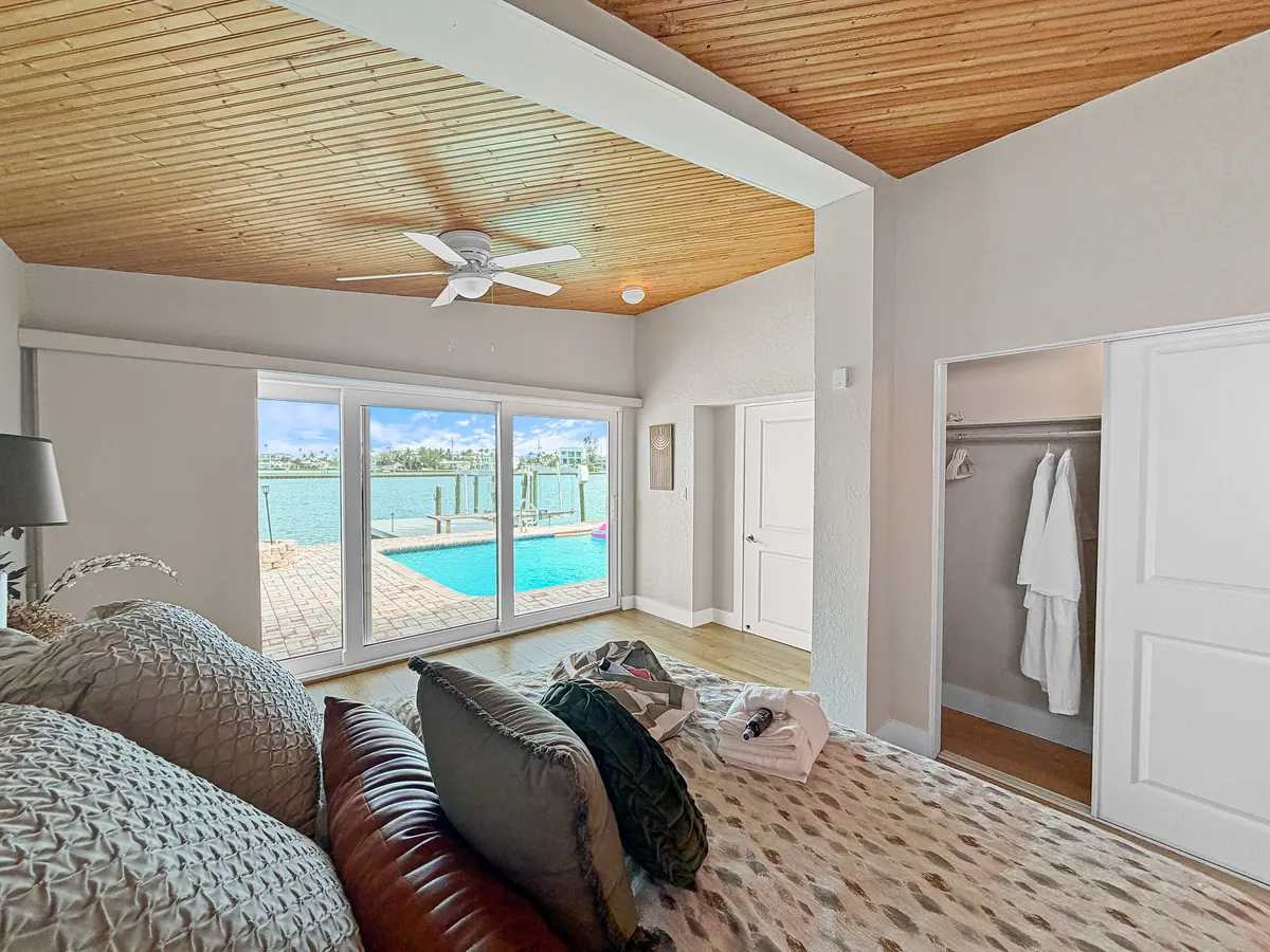 Bedroom with soft layered bedding and sliding doors framing the pool and water beyond.