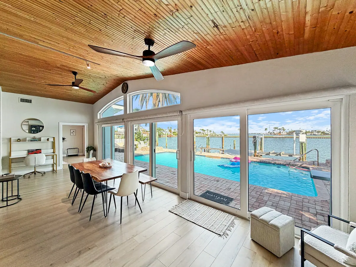 Dining table for eight beneath a timber-clad vaulted ceiling, with sliding doors opening onto the pool deck.