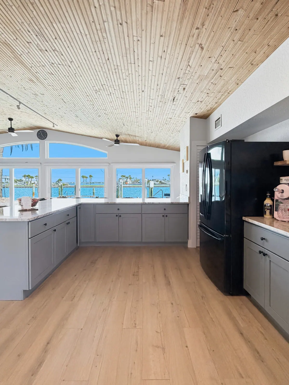Kitchen with grey cabinetry and a run of windows looking out across the water.