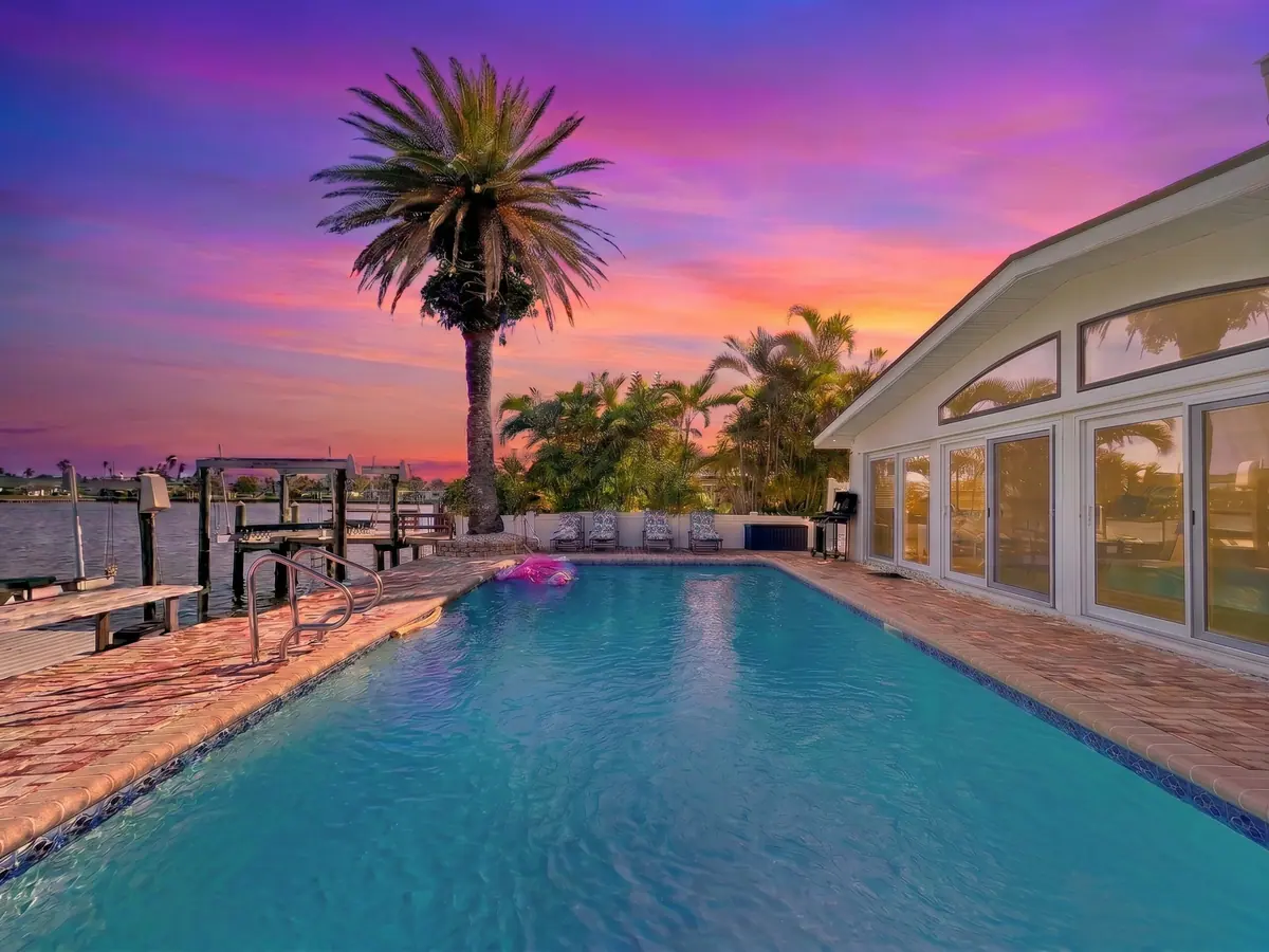 The long waterfront pool at sunset, a tall palm silhouetted against a pink and violet sky.