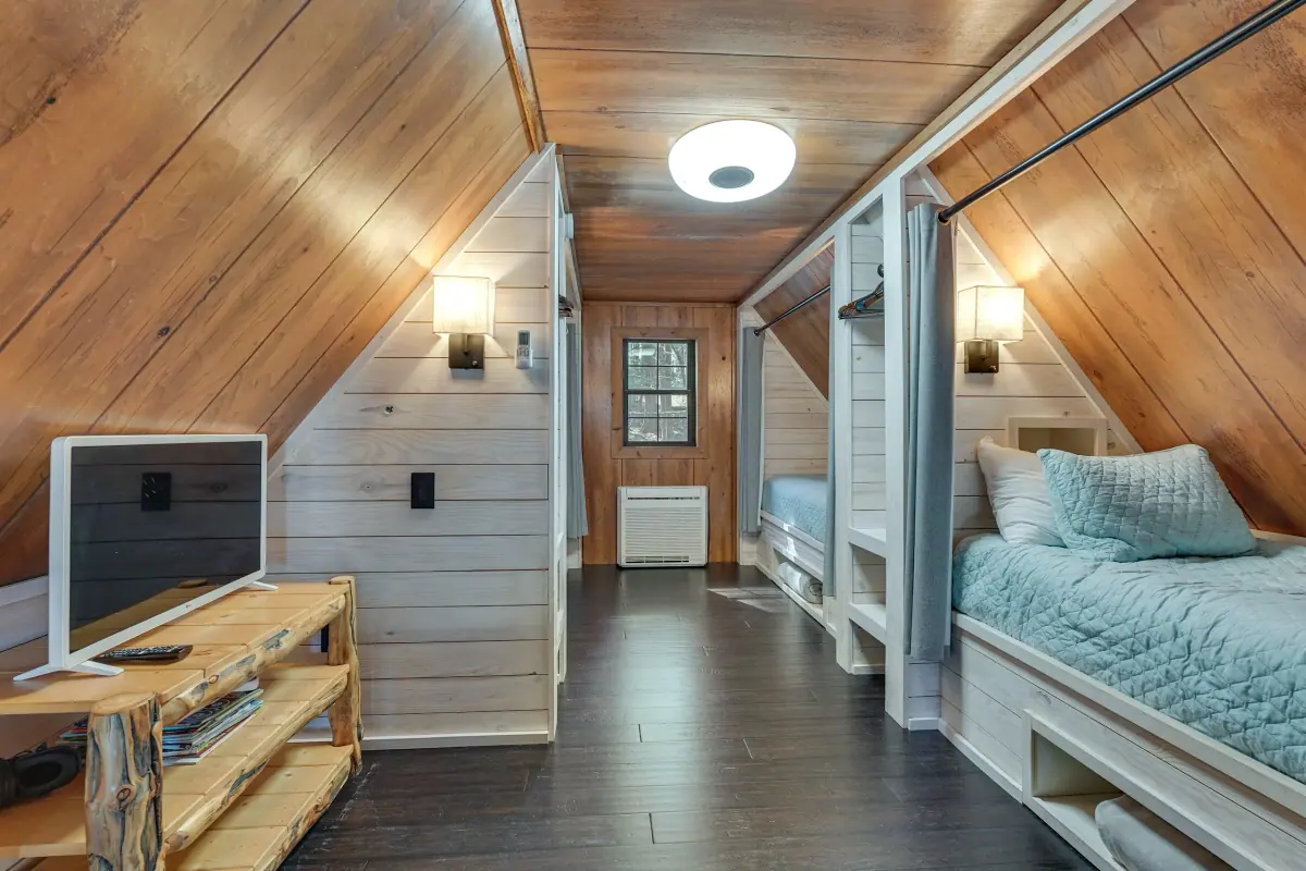 Loft bedroom tucked under the A-frame slope, with beds arranged along the low pine walls.