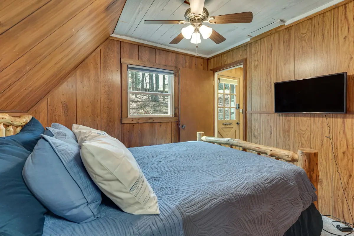 Main-level bedroom with a queen bed, pine-panelled walls and a wall-mounted television.