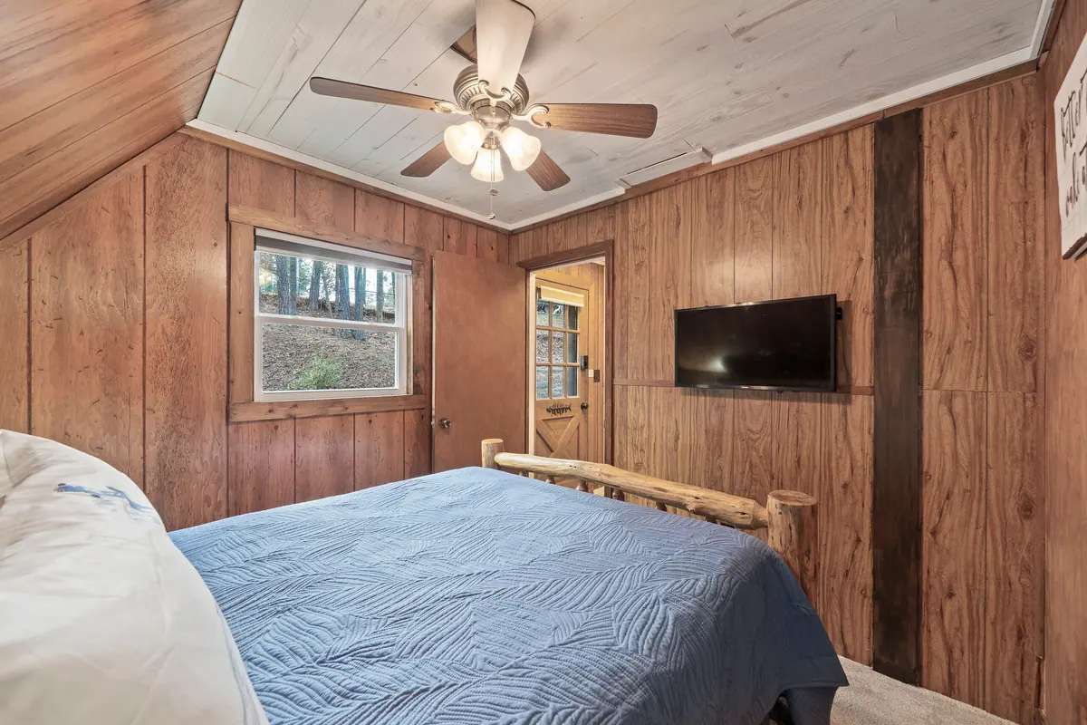 Second bedroom with a wall-mounted television and warm timber panelling.