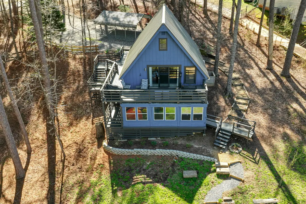 The blue A-frame cabin among tall pines, its steep roofline running to the ground and a deck wrapping the front.