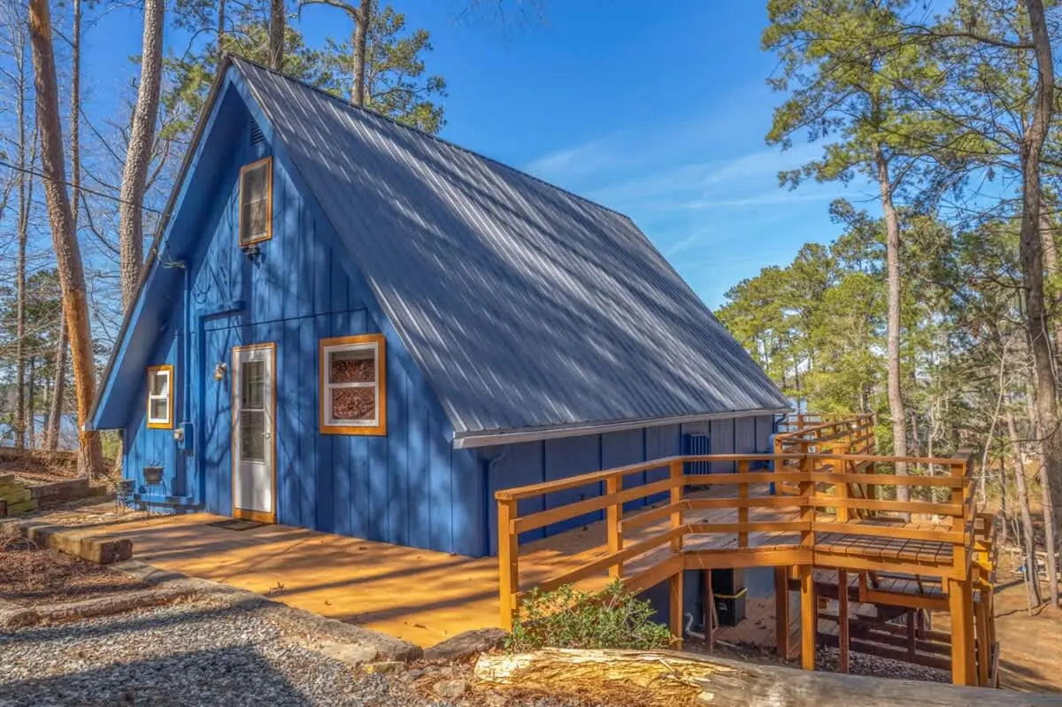 The A-frame from the side, with its timber stair and wraparound deck among the pines.