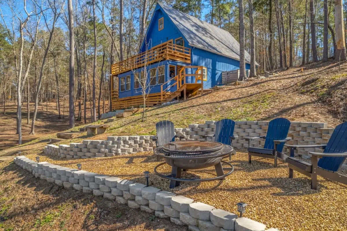 Terraced fire pit ringed by blue Adirondack chairs on the slope between the cabin and the water.