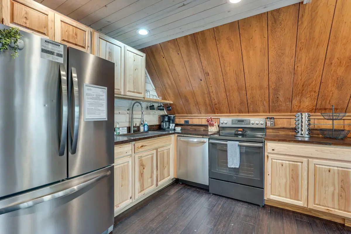 Kitchen with light wood cabinetry, stainless refrigerator and range, tucked under the sloping A-frame wall.