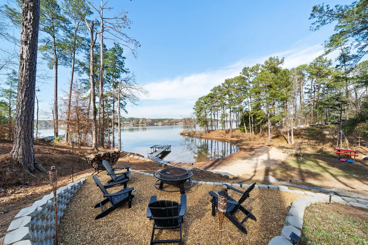 Adirondack chairs drawn around a fire pit above the shoreline, with the dock, the sandy cove and Lake Sinclair opening out behind.