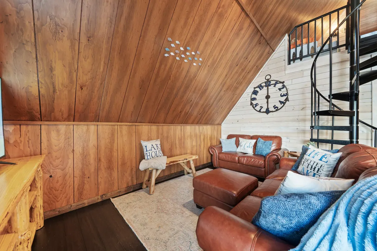 Pine-lined living area with brown leather sofas and a spiral staircase rising to the loft.