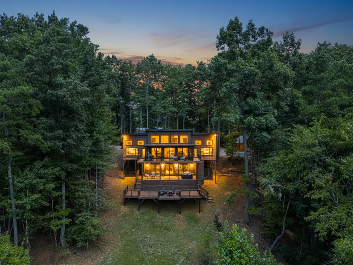 Aerial view at dusk of the cabin lit from within, its stacked decks glowing among tall trees.