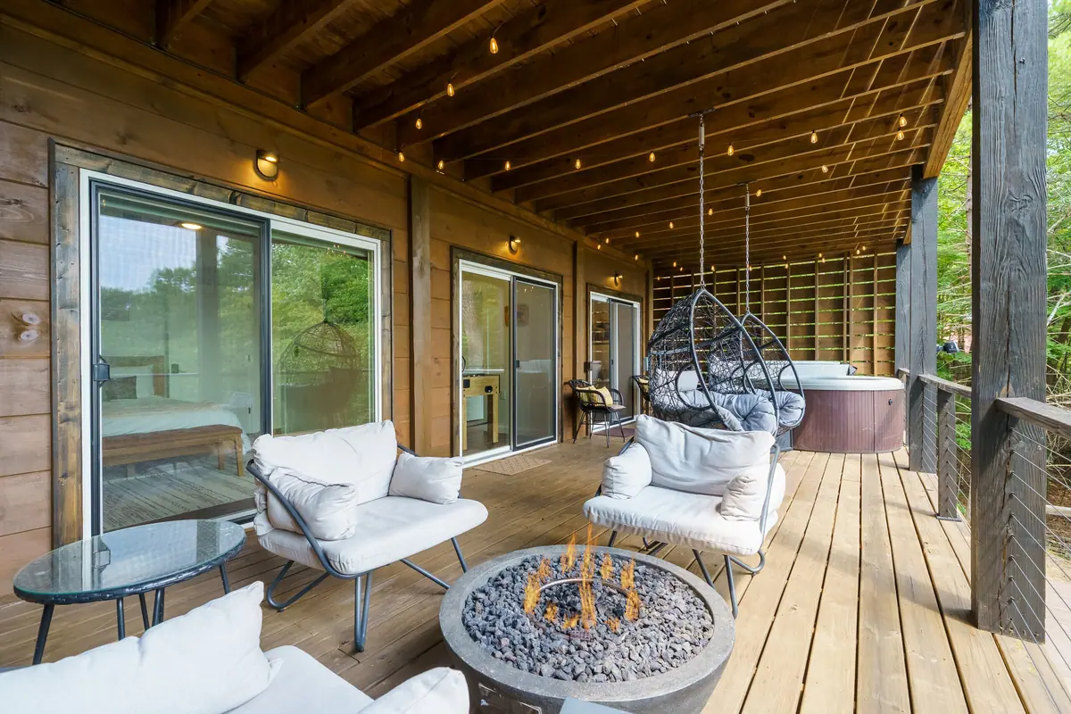 Covered deck with a hot tub, a fire bowl and a hanging chair, looking out into the trees.