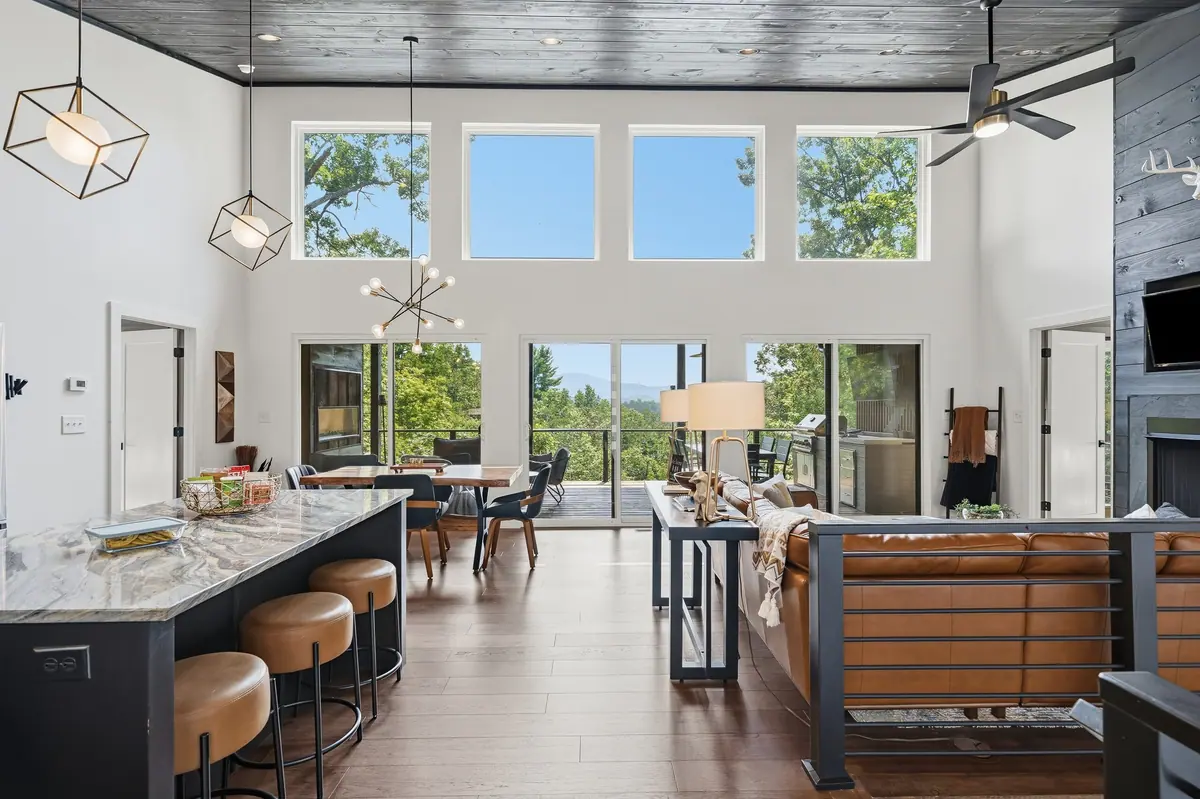 Open living and dining space under a tall vaulted ceiling, with a wall of glass onto the deck.