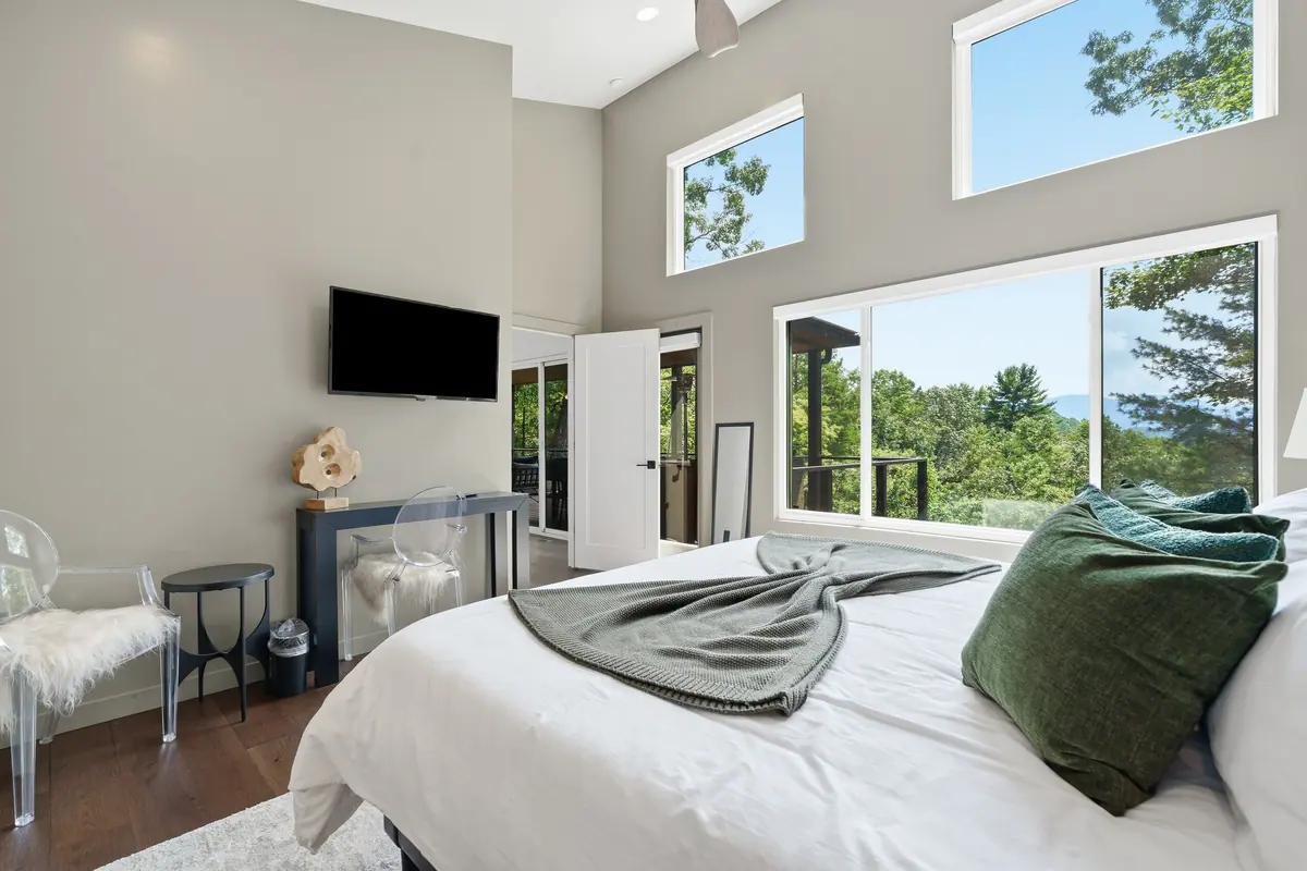 Bedroom with a king bed, green accent cushions and windows opening onto the ridge view.