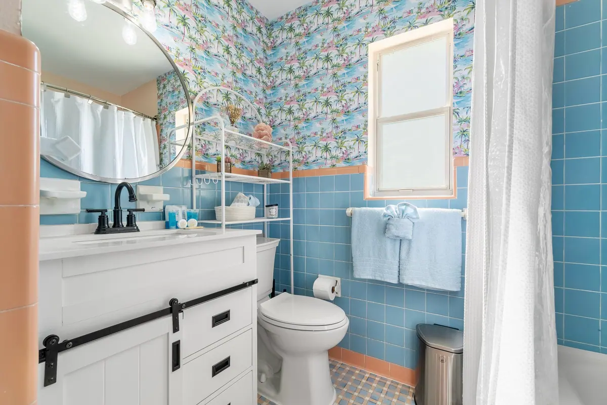 Bathroom with original blue tile, a curved vanity and a botanical-print wall.