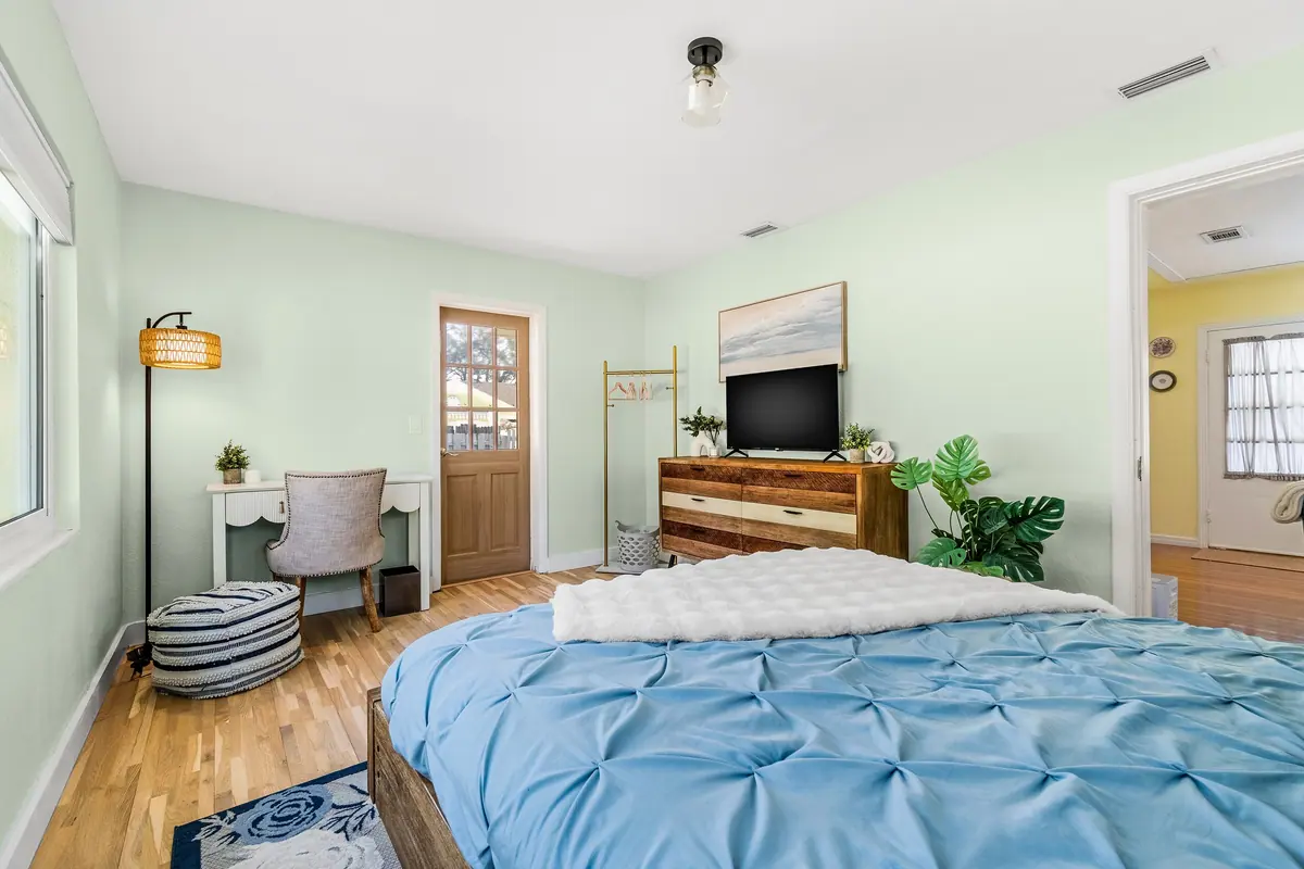 Bedroom in soft green with a queen bed, a wall-mounted television and a slim writing desk.