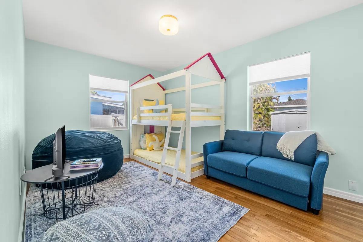 Children’s room with a house-frame bunk bed, a blue sofa and a beanbag on a patterned rug.