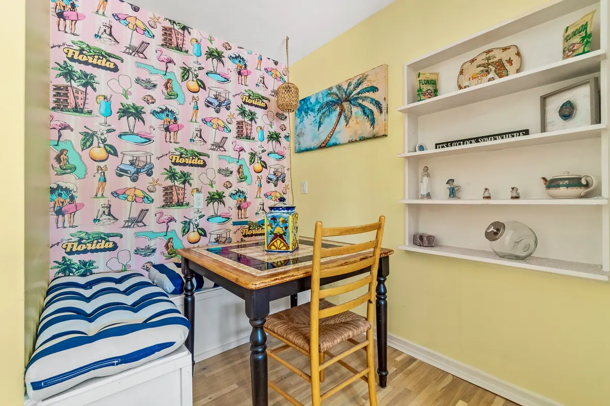 Breakfast nook with a vintage Florida souvenir-print wallpaper, a built-in bench with striped cushions and open shelving.