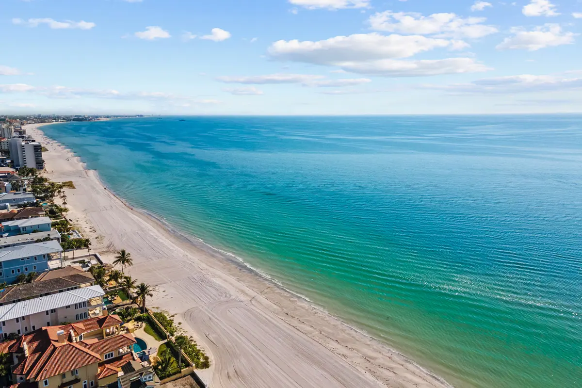 Aerial view along the Gulf coastline, turquoise water shading to deep blue past a band of white sand.