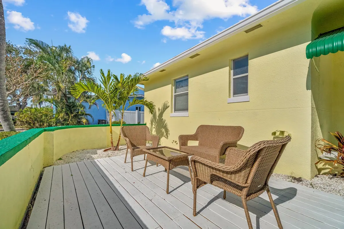 Wicker armchairs and a side table on the back deck, with palms and the neighbouring rooftops beyond.
