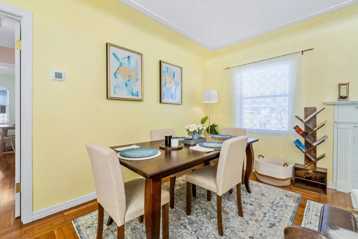 Dining table for four with upholstered chairs, framed prints and a bright window behind.