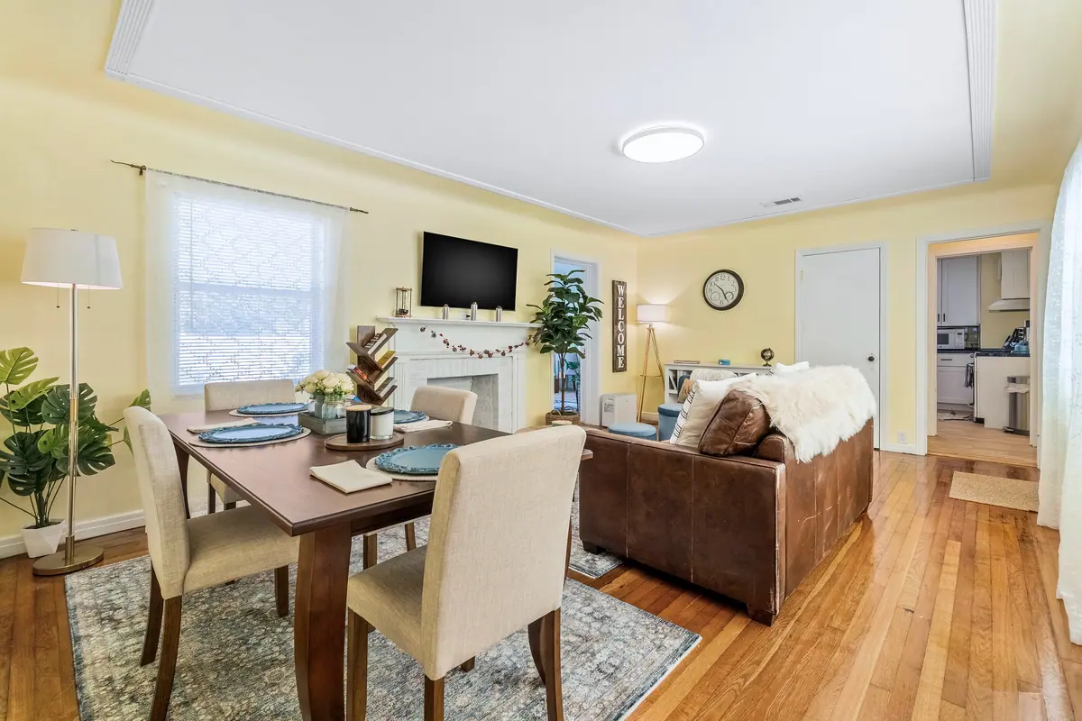 Open dining and living area with a table for four, a leather sofa and bright windows.