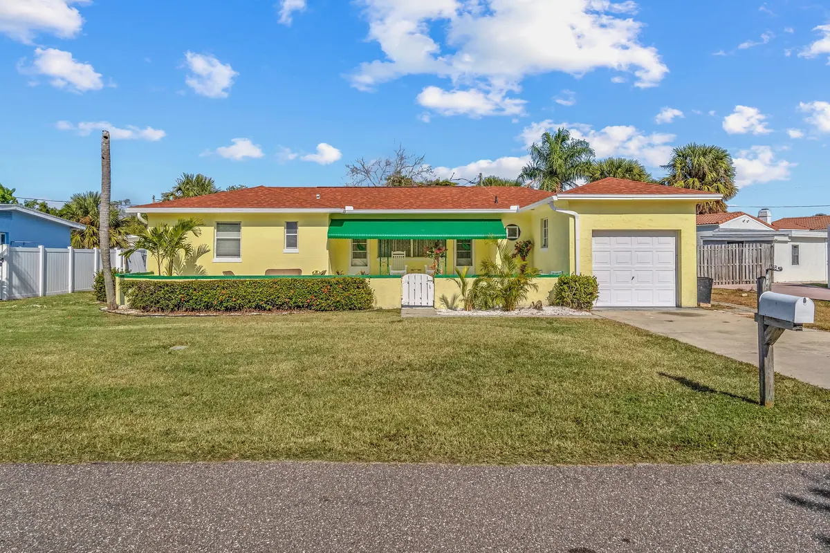 The butter-yellow cottage with its red tile roof and green trim, set back behind a wide lawn and palms.