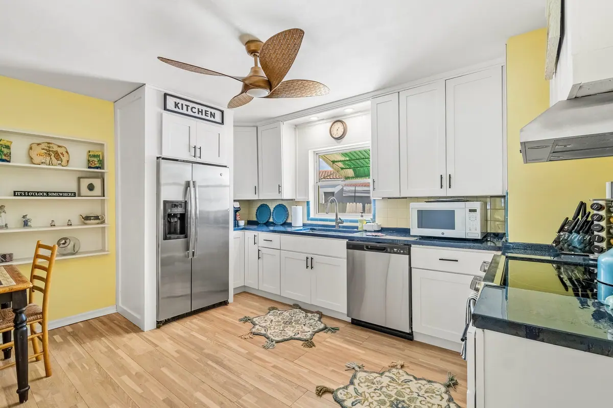 Cottage kitchen with white cabinetry, deep blue counters, stainless appliances and a green-striped window awning.