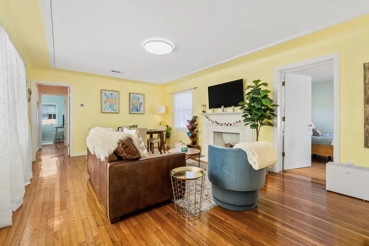 Living room in warm yellow with a leather sofa, a swivel armchair and light pouring through to the hallway beyond.