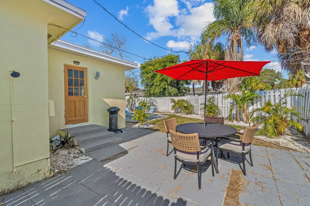 Side patio with a bistro table under a red umbrella, screened by a row of palms.