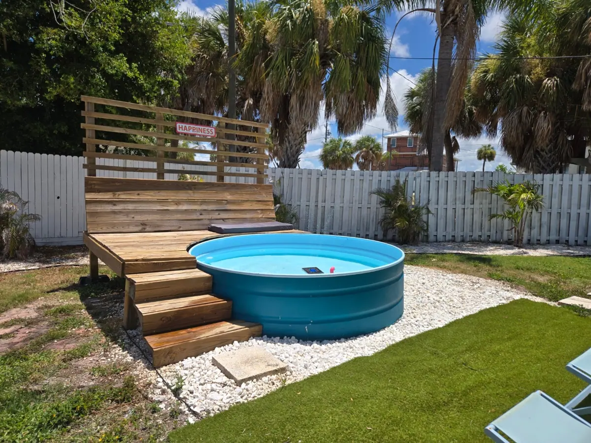 Round galvanised plunge pool set into a timber deck in the fenced backyard, framed by palms.