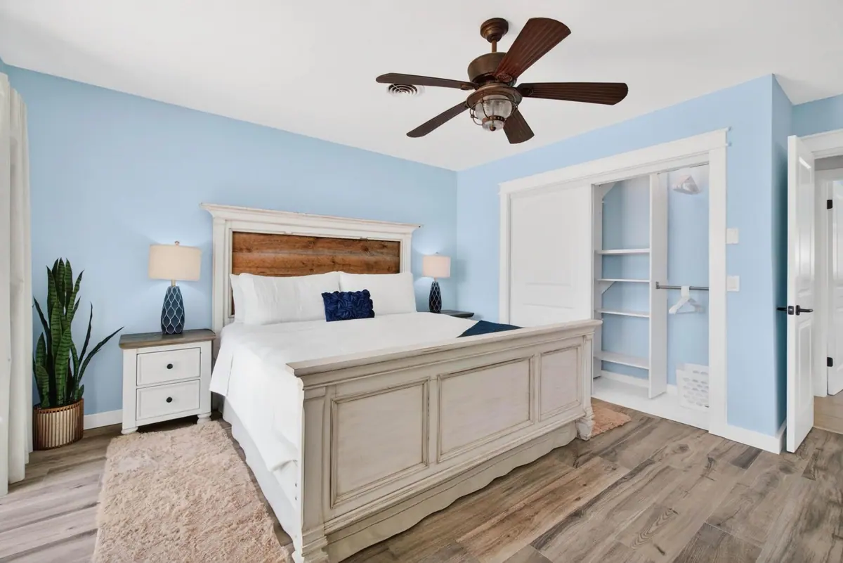 Guest bedroom with a queen bed, pale blue walls and a ceiling fan.
