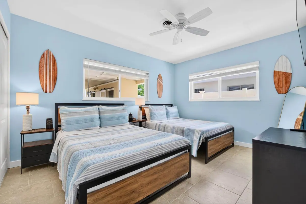 Guest bedroom with two beds dressed in striped linens and a surfboard-motif wall.