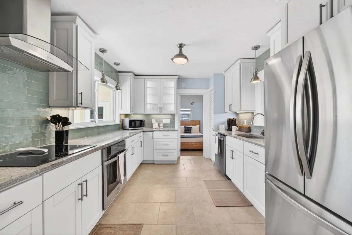 Galley kitchen in white cabinetry with stone counters, stainless appliances and a sea-glass tiled backsplash.