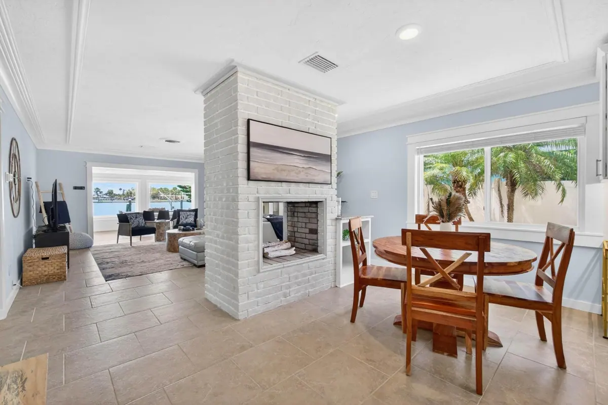 Open living and dining space anchored by a whitewashed brick fireplace, with water visible through the far windows.
