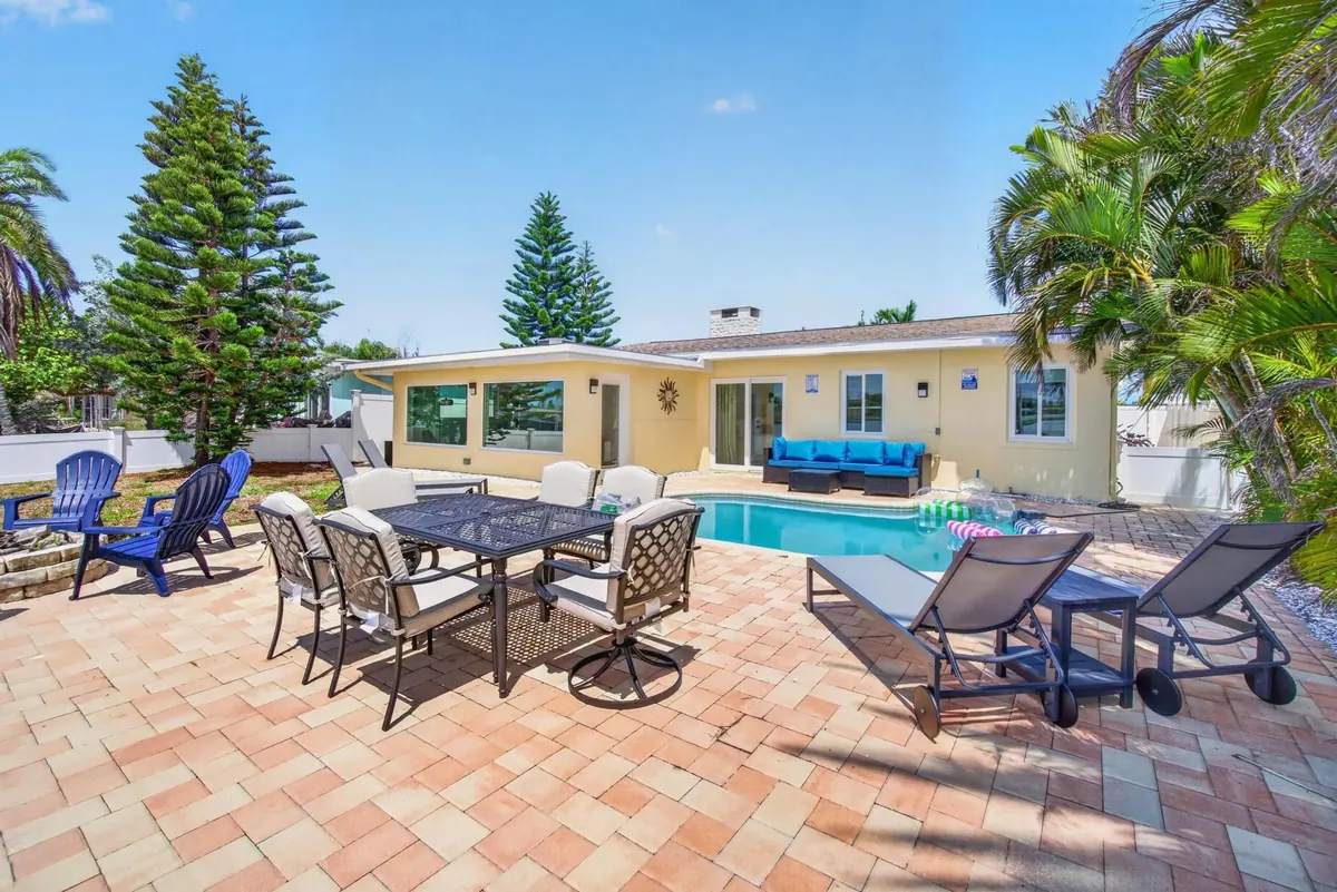 Paver patio beside the pool with an outdoor dining set, loungers and the house behind.