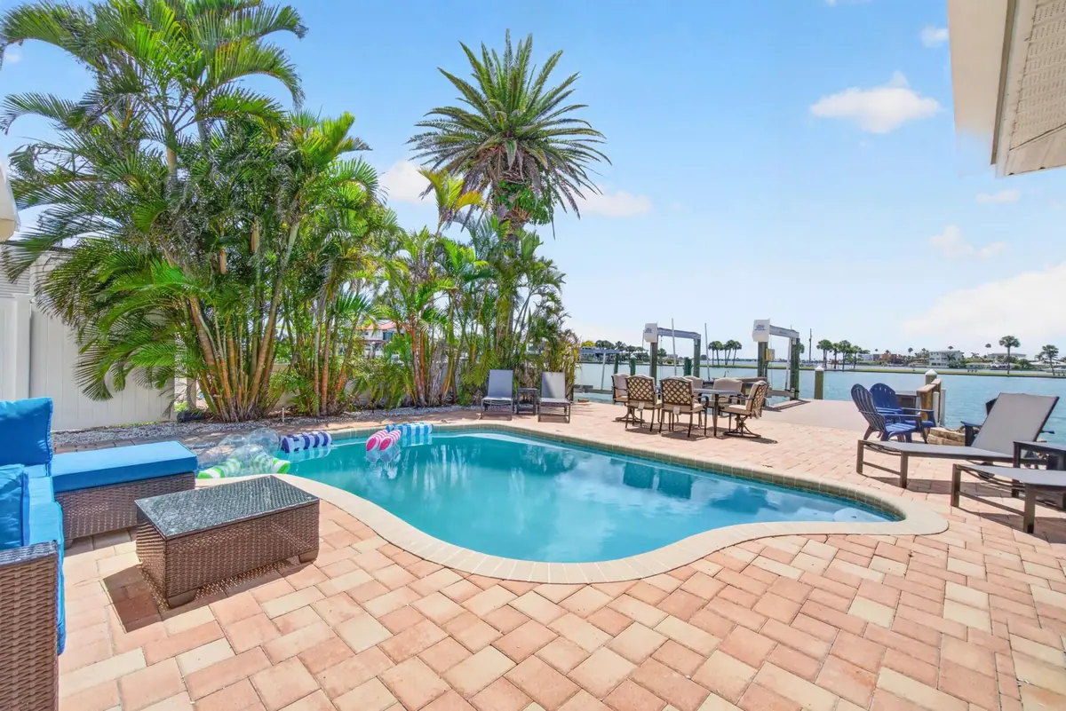 Free-form pool on a brick paver patio behind the house, framed by tall palms with the waterfront cove just beyond.