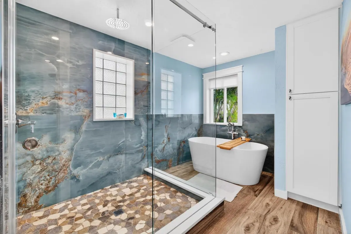 Primary bathroom with a freestanding soaking tub and an oversized glass walk-in shower over a pebbled floor.
