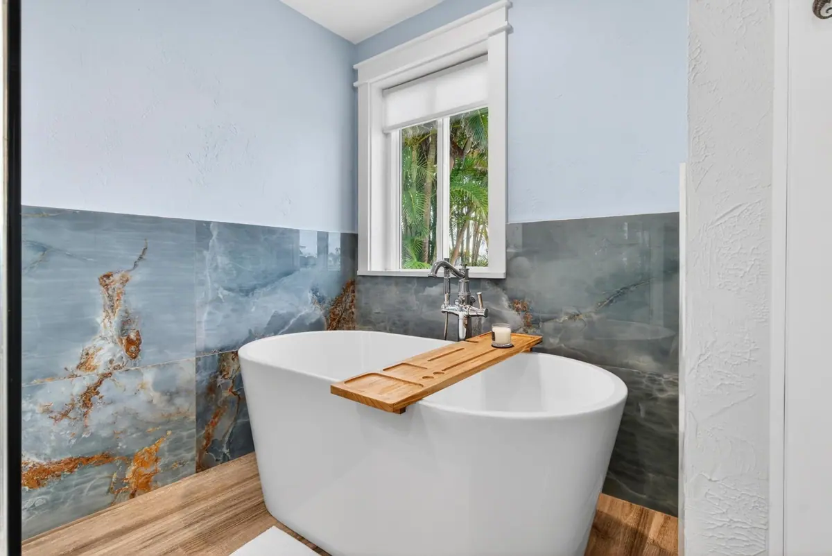 Freestanding soaking tub with a timber bath caddy, set against a dramatic veined stone wall.