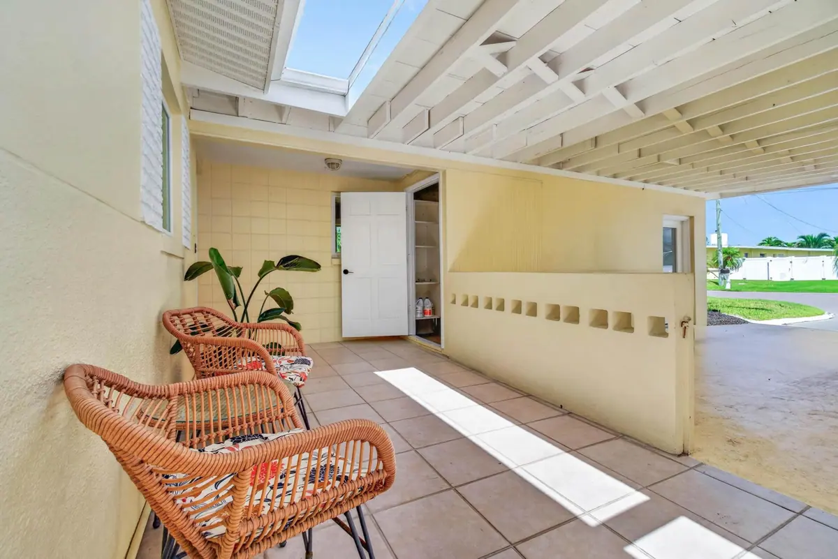 Tiled sunroom with woven rattan chairs and a wall of windows opening onto the lawn and water.