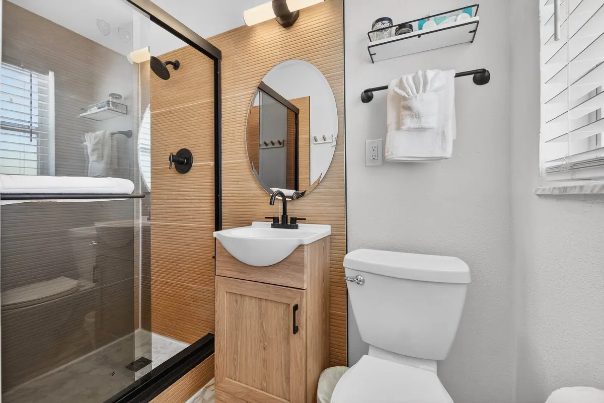 Bathroom with a glass walk-in shower, timber-look tiling and a round mirror above a slim vanity.