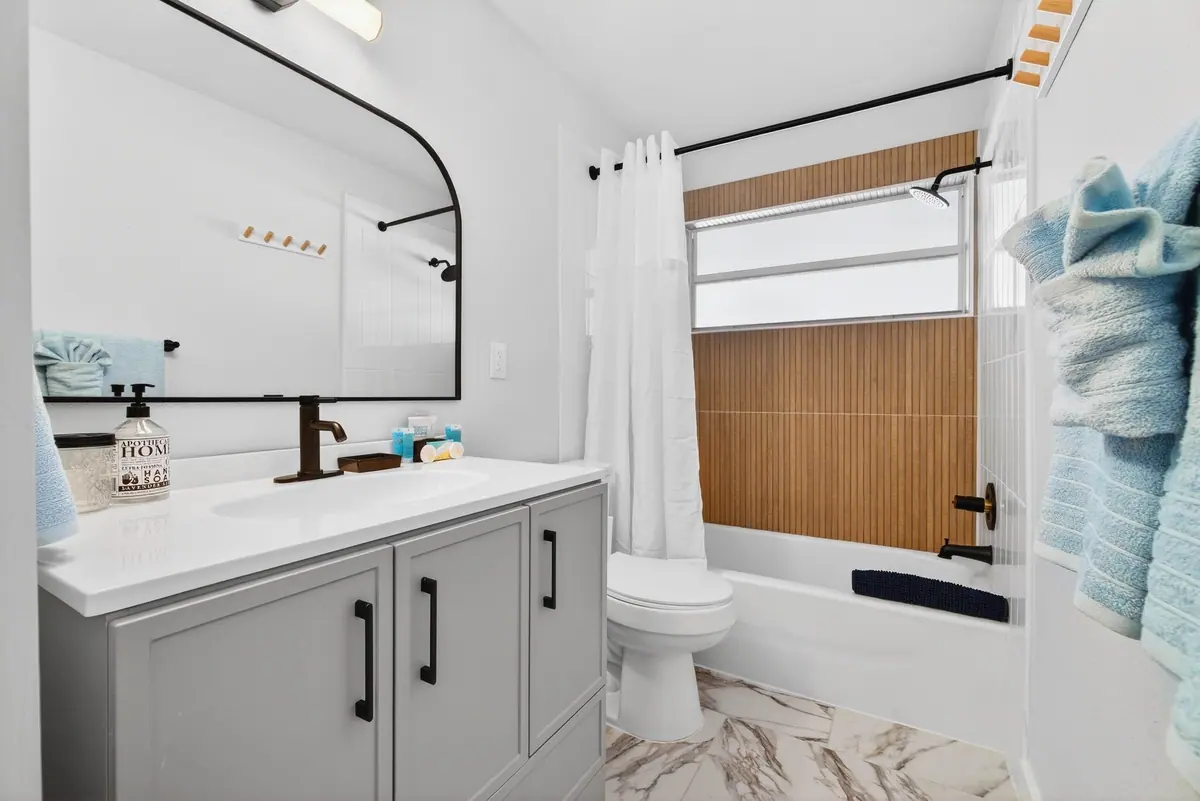 Second bathroom with a grey vanity, arched mirror and a tub-shower behind a curtain.