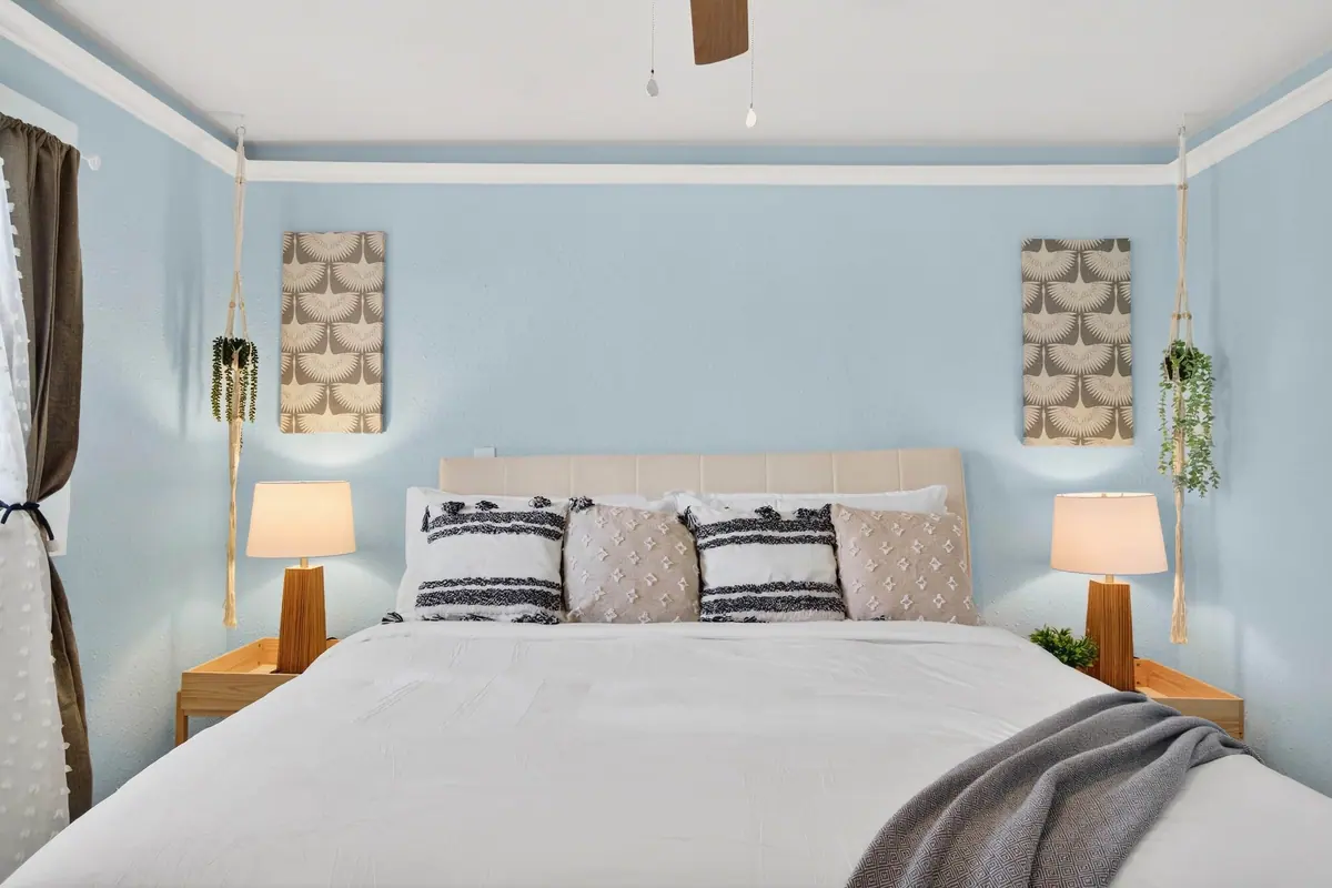 Bedroom with a king bed, upholstered headboard and matching bedside lamps against pale blue walls.