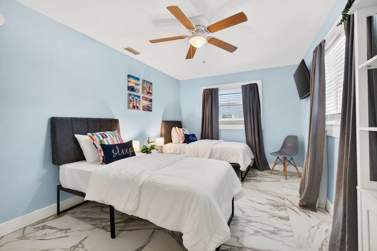 Bedroom arranged with two twin beds, a desk chair and a surf-themed cabinet.