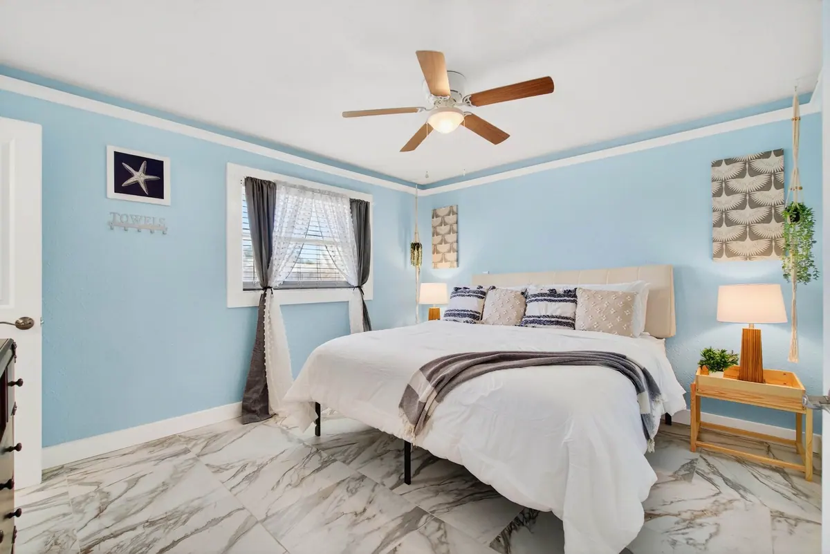 Second king bedroom with a ceiling fan, marble-look flooring and a window framed by curtains.